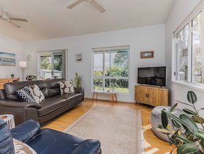 A modern living room with a leather sofa, a television, and large windows offering a view of the outdoors. - Pottsville Coastal Retreat (Pottsville)