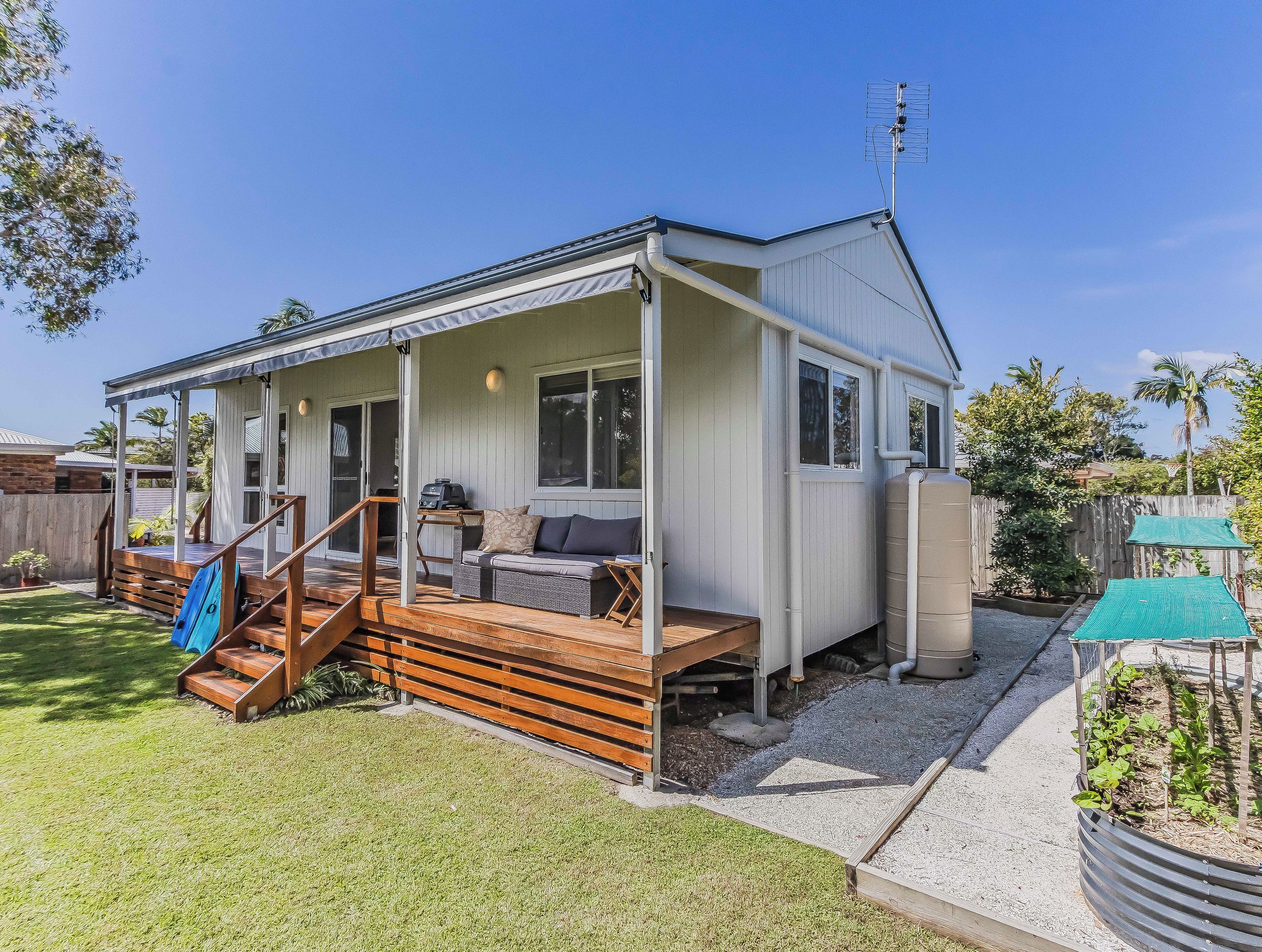 A single-story house with a covered porch, a barbecue grill, and a small garden area.
