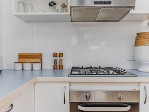 Een keuken met een gasfornuis, witte kastjes en een houten hoofdbord.