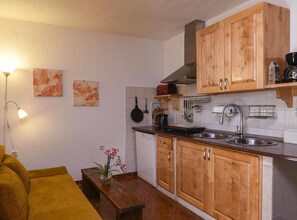 A compact kitchen with wooden cabinets, a countertop, a sink, and a stove. There is a small dining area with a yellow sofa and a table. - Villa Vida - Orebić (Orebic)