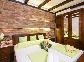 A bedroom with a stone wall, wooden headboard, a bed with green bedding, and a wooden wardrobe. - Villa Vida - Orebić (Orebic)