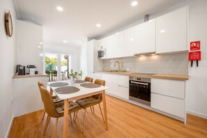 A modern kitchen with white cabinets, a wooden countertop, and a dining area with a white table and brown chairs. - GuestReady-Charming Retreat in Alcochete (Alcochete)