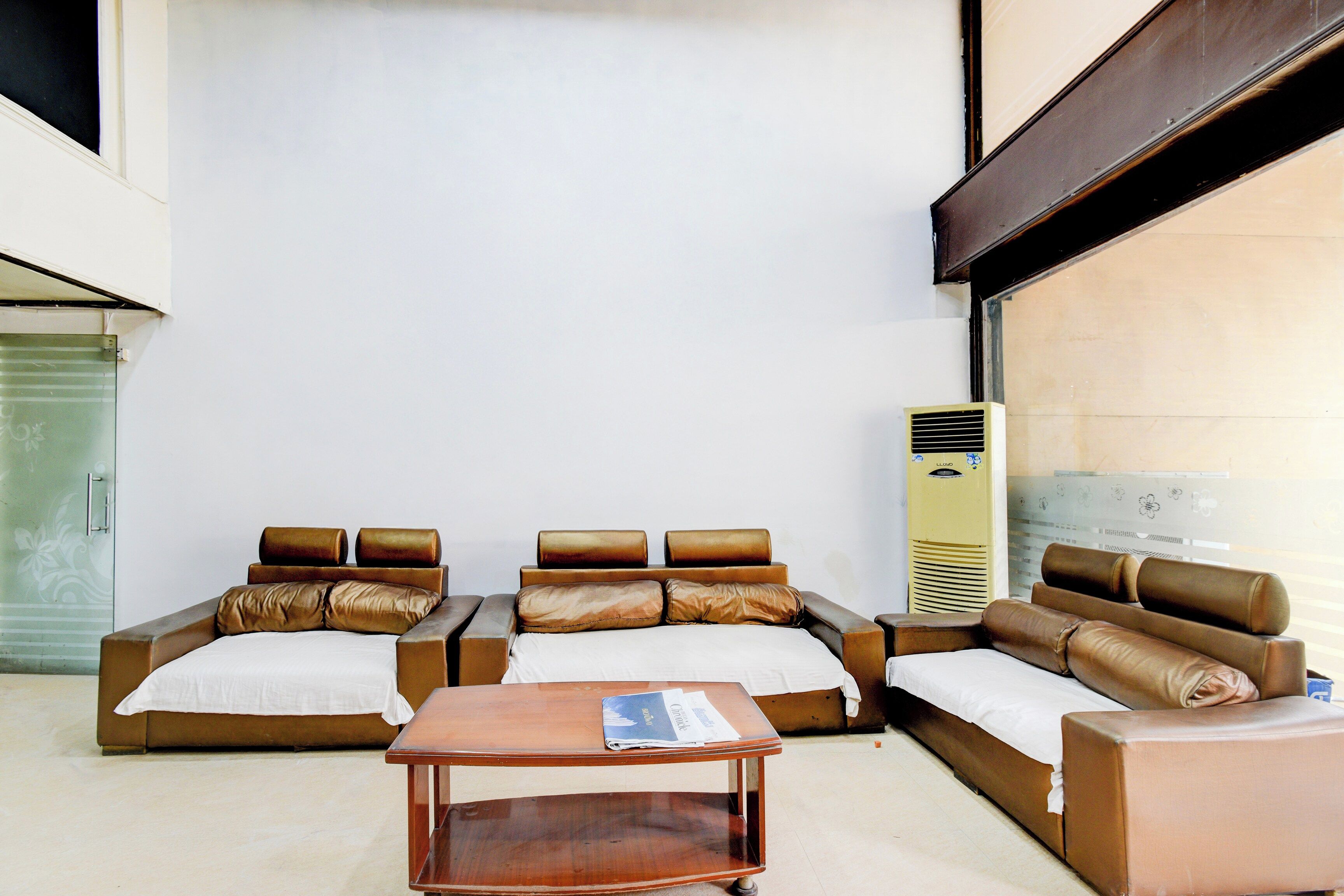 A hotel room with a sofa set, a wooden side table, and a standing air conditioner.