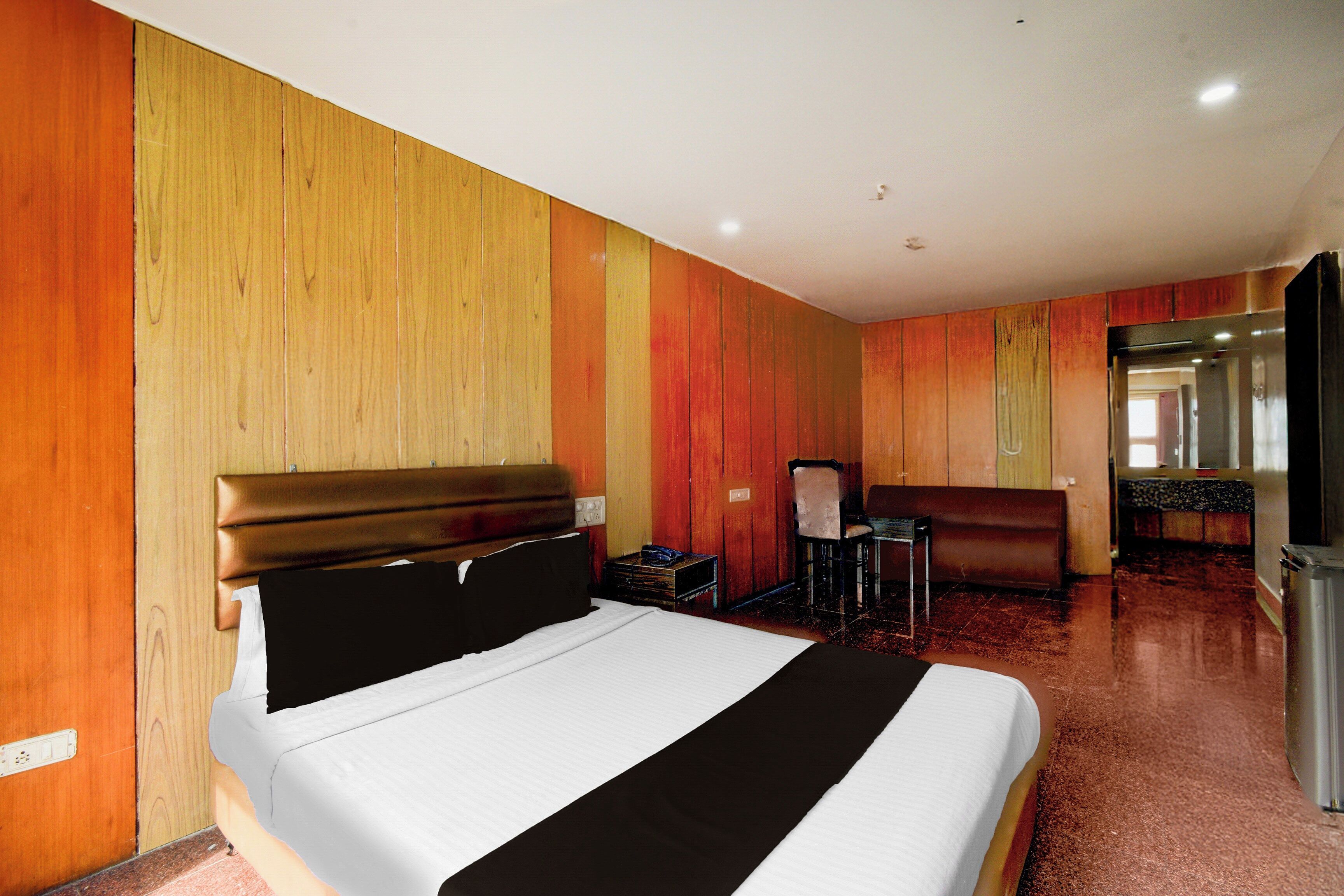 A hotel room with a bed, a desk, a chair, and a mirror.