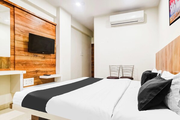 Une chambre d’hôtel avec un lit, un téléviseur fixé au mur, un appareil de climatisation et un tableau accroché au mur.