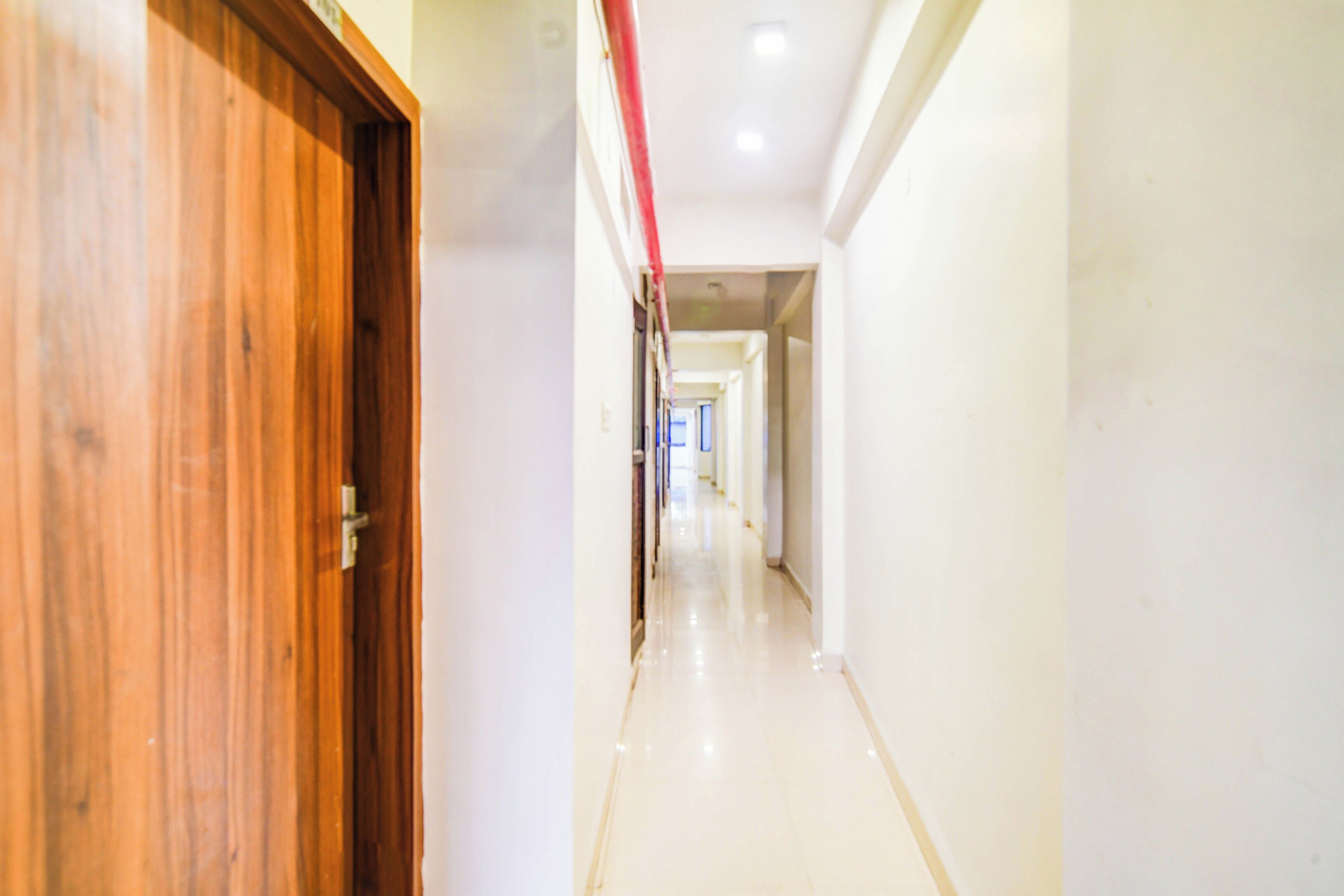 A corridor with a wooden door on the left, leading to a hallway with a tiled floor and white walls.