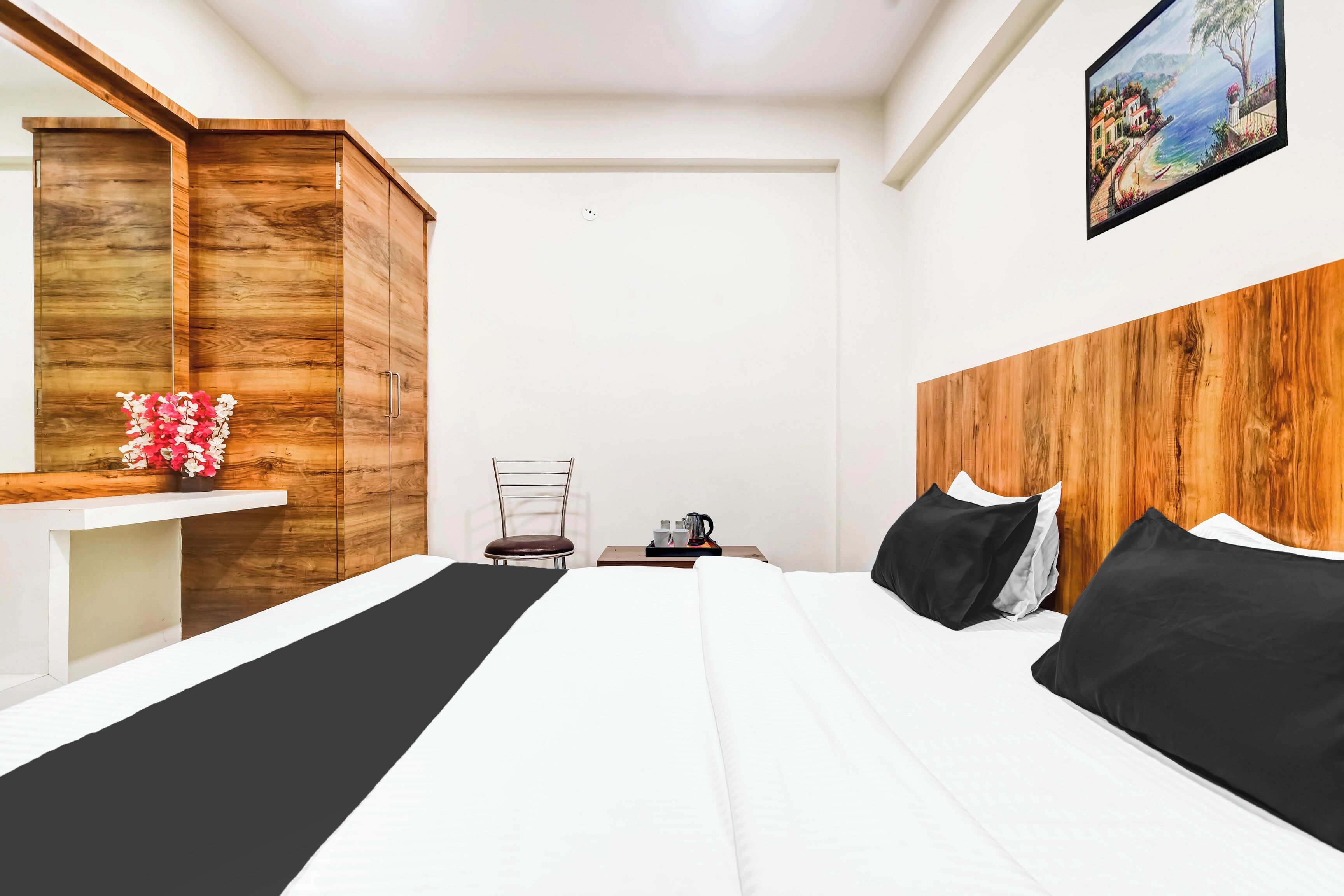 Una habitación de hotel con una cama, cabecera de madera, mesita de noche, una silla y un cuadro en la pared.