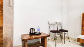 Quarto pequeno com uma mesa de madeira, duas cadeiras de metal, uma garrafa de água e uma chaleira.