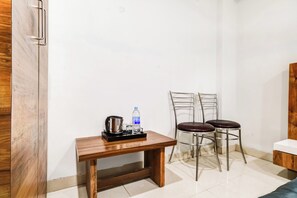 Une petite pièce avec une table en bois, deux chaises en métal, une bouteille d’eau et une bouilloire.