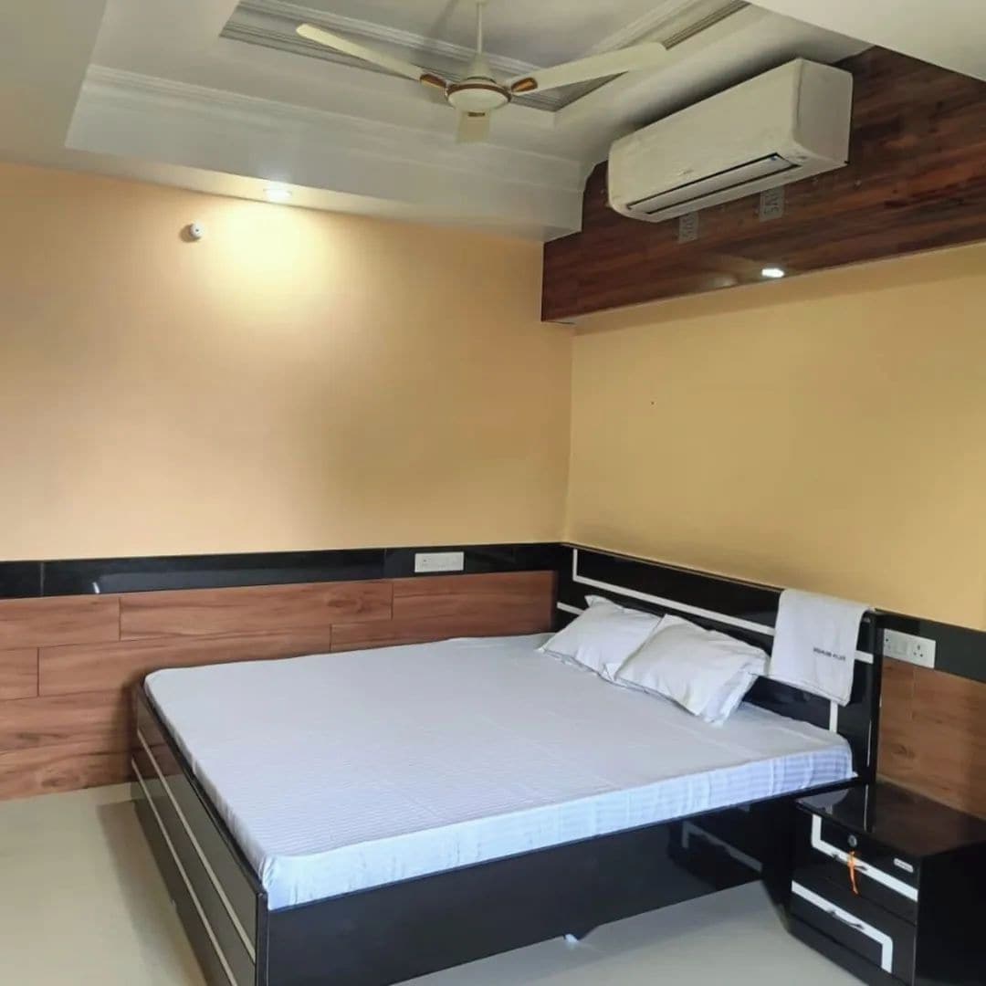 A bedroom with a bed, a nightstand, a wall-mounted air conditioner, and a ceiling fan.