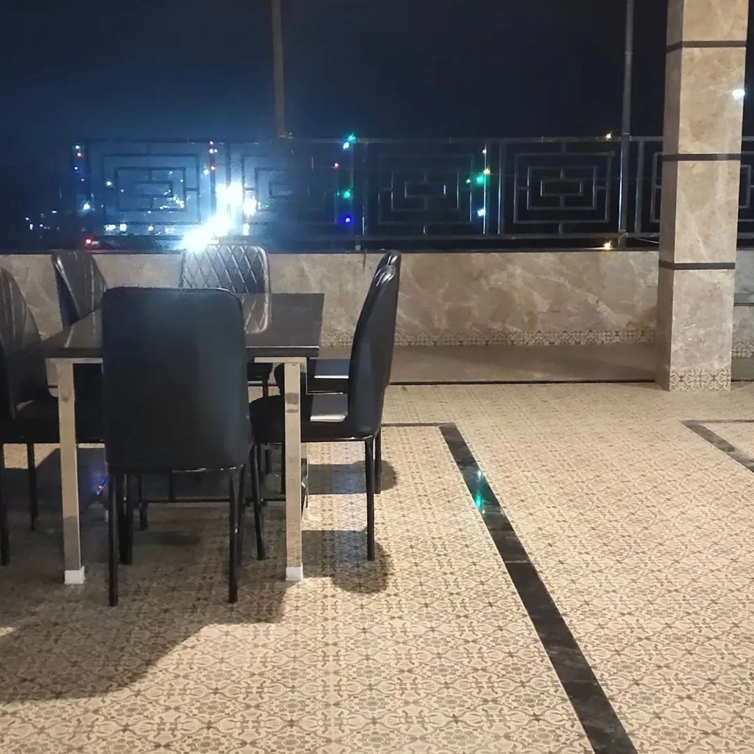 Un área de comedor al aire libre con una mesa y sillas, piso con diseño y vistas a luces de la ciudad al fondo.