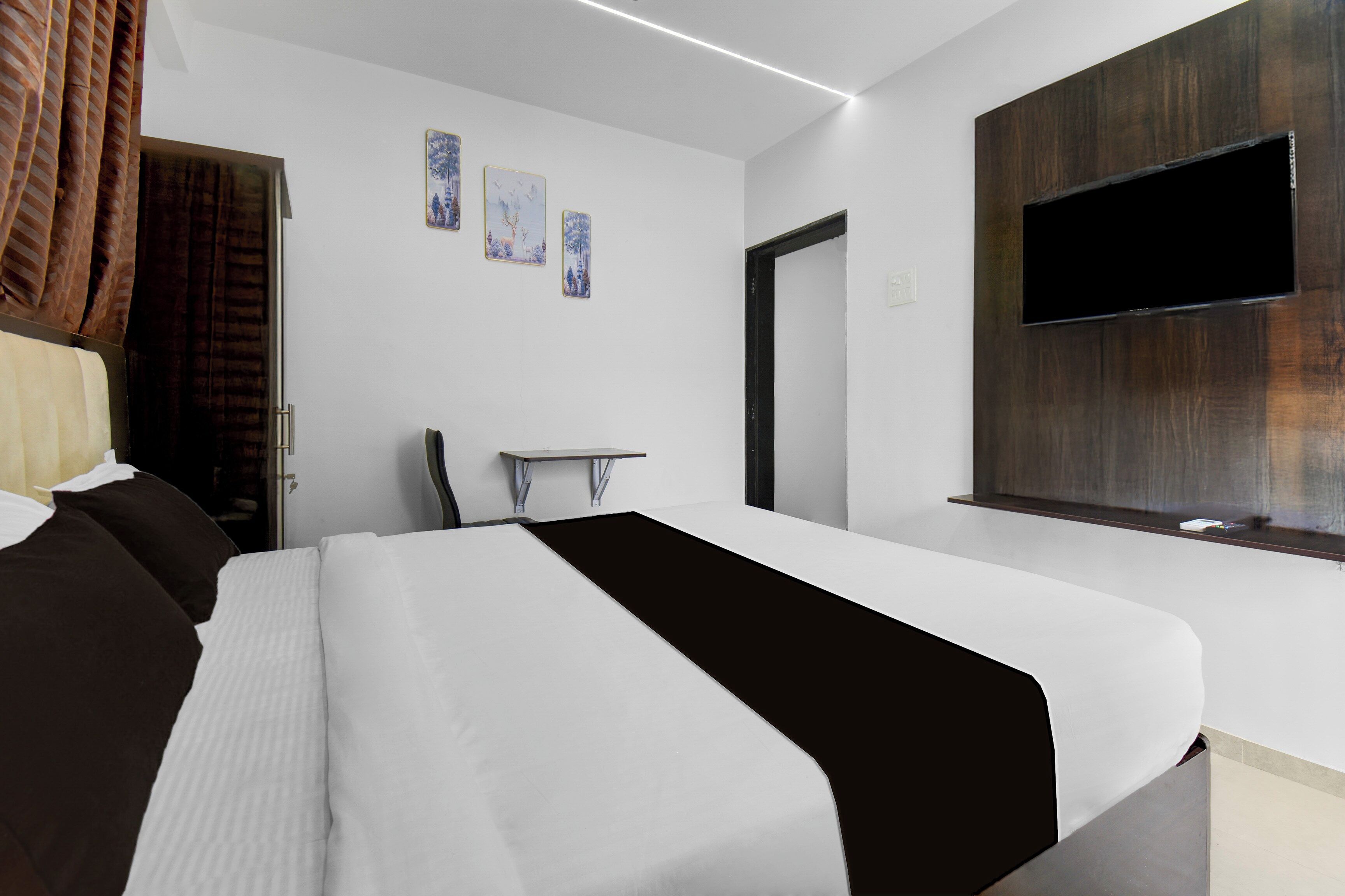 Habitació d'hotel moderna amb un llit gran, televisió de pantalla plana penjada a la paret i una porta que condueix a una altra habitació.