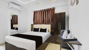 A modern hotel room with a bed, a desk with a kettle, and a minibar.