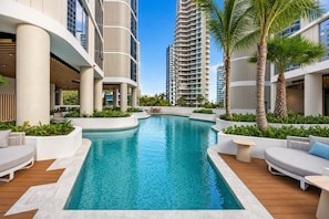 A swimming pool with a curved design, surrounded by white planters and palm trees. - Sunrise Ocean Escape - Lagoon Main Beach (Main Beach)