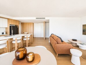 A modern kitchen with a central island, bar stools, and a sofa in a living area with a round coffee table. - Sunrise Ocean Escape - Lagoon Main Beach (Main Beach)