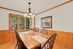 A dining room with a wooden table, chairs, a vase with flowers, and a painting on the wall. - Easy Mornings Cabin  Hot Tub, Stone Fireplace & Stream  Pet-Friendly  Boone (Vilas)