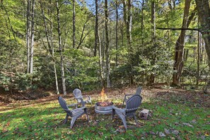 An outdoor seating area with chairs and a fire pit surrounded by a forest. - Easy Mornings Cabin  Hot Tub, Stone Fireplace & Stream  Pet-Friendly  Boone (Vilas)