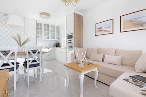 Ein modernes Wohnzimmer mit einem beigen Sofa, einem Holztisch und einem Essbereich mit weißen Stühlen und einem weißen Tisch.