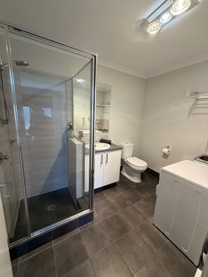A modern bathroom with a glass shower enclosure, a toilet, a sink, and a washing machine. - comfortable 1 bedroom 1 bathroom unit attached to main house completely private. (Wellard)