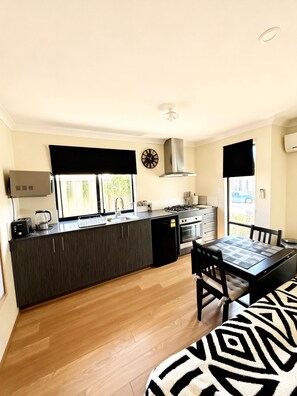 A compact kitchen with a central island, a dining table with chairs, and a view of the outdoors. - comfortable 1 bedroom 1 bathroom unit attached to main house completely private. (Wellard)