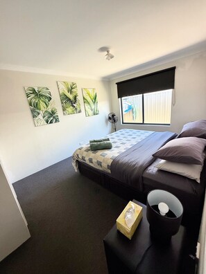 A bedroom with a bed, a bedside table, a fan, and a window with blinds. - comfortable 1 bedroom 1 bathroom unit attached to main house completely private. (Wellard)
