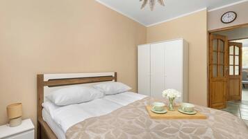 Quarto com cama, mesa de cabeceira, abajur, guarda-roupa e relógio na parede.