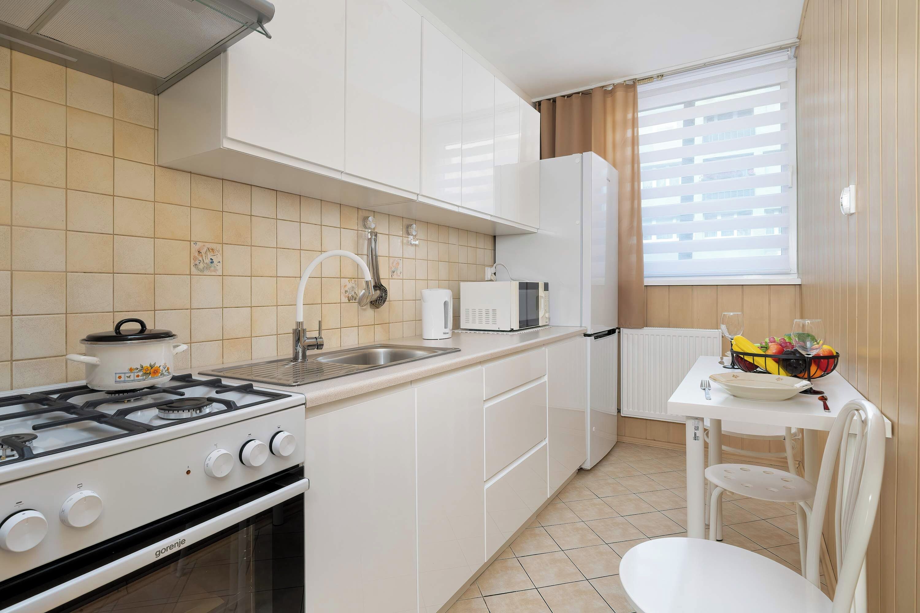 A compact kitchen with white cabinets, a gas stove, a microwave, and a small dining area with a table and chair.