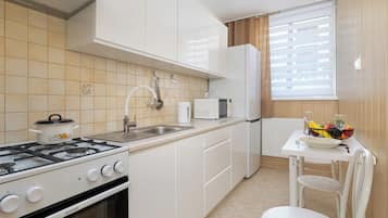 A compact kitchen with white cabinets, a gas stove, a microwave, and a small dining area with a table and chair.
