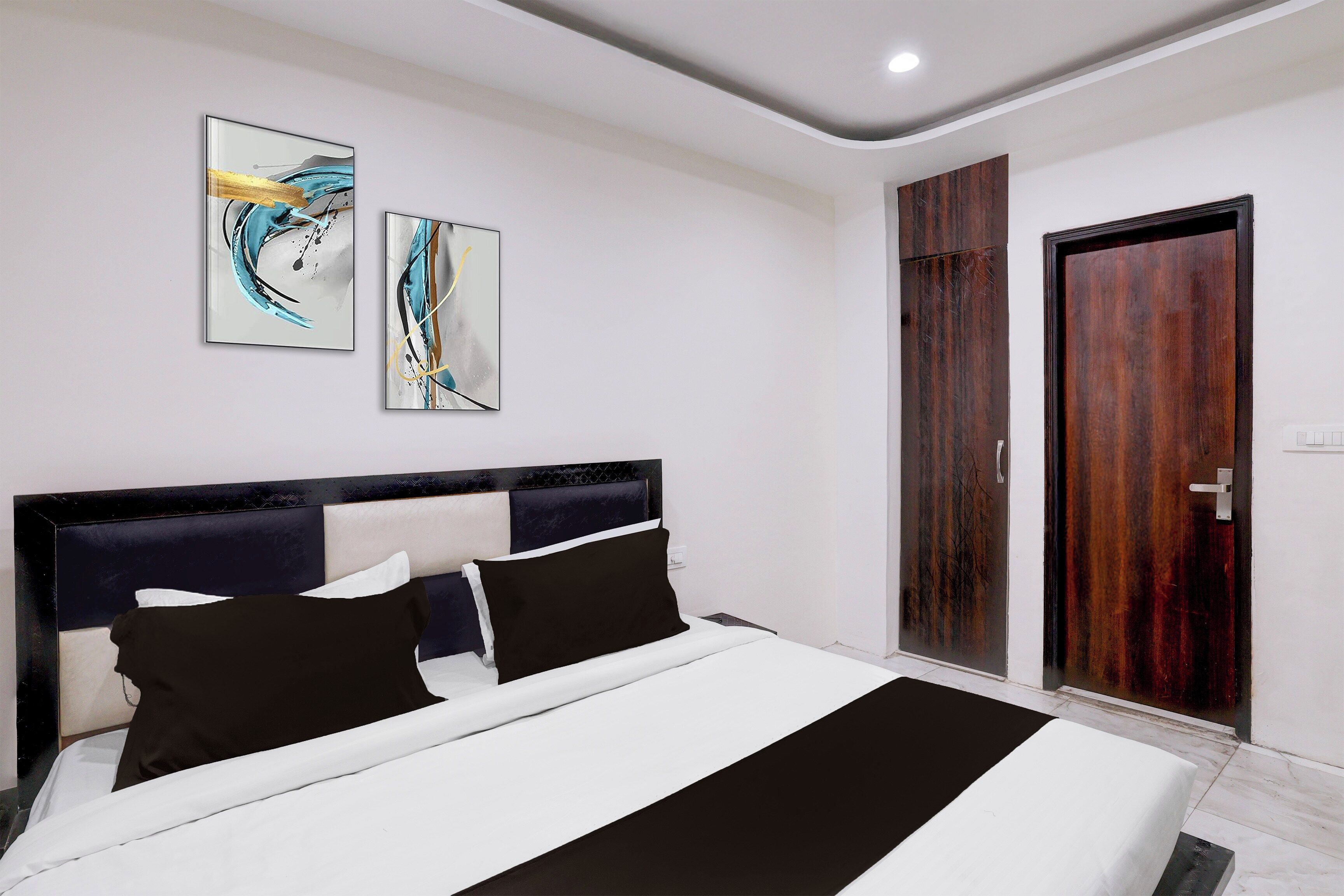 Une chambre moderne avec un lit, deux tableaux abstraits, une armoire en bois et une porte.