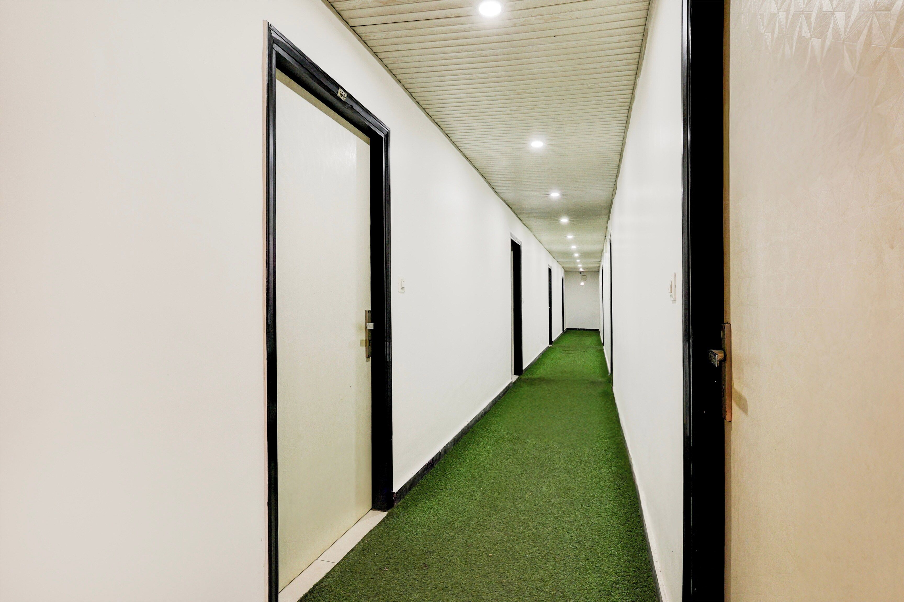 Un pasillo con paredes blancas, puertas negras y alfombra verde.