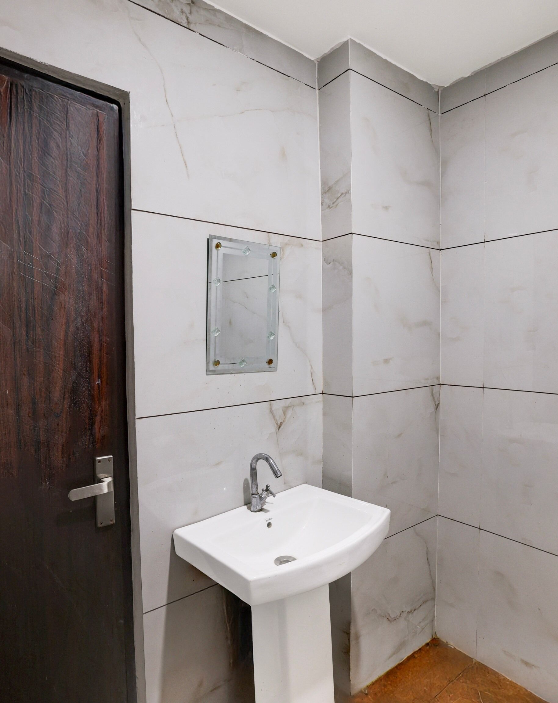 Un baño con un lavamanos blanco, una puerta de madera oscura y baldosas de mármol blanco.