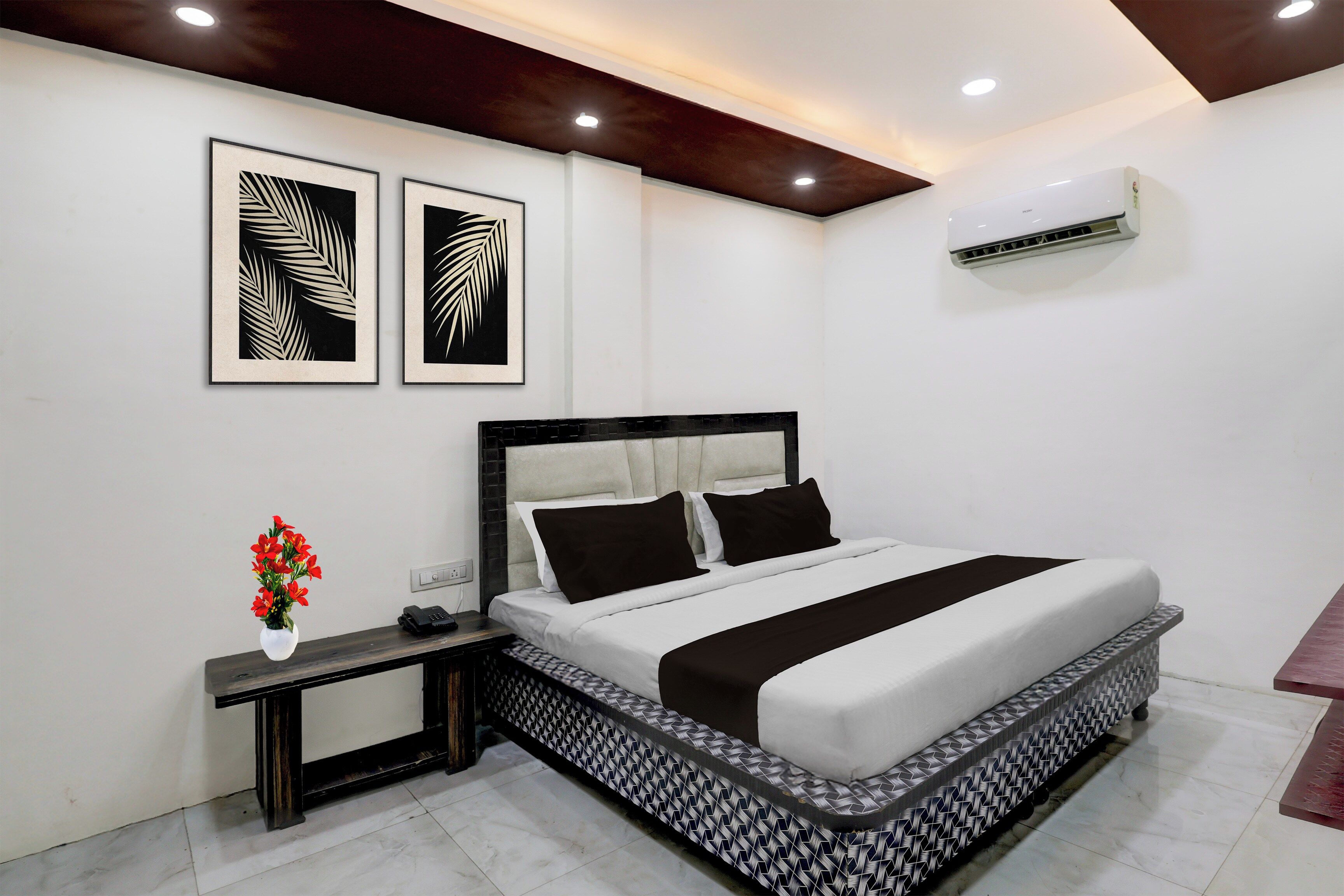 Une chambre à coucher moderne, avec un lit, des tables de chevet, une petite table, un vase avec des fleurs et deux œuvres d’art encadrées accrochées au mur.