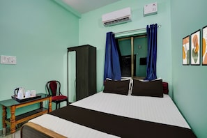 Quarto de hotel com cama, escrivaninha com chaleira e chávenas, uma cadeira e ar condicionado na parede.