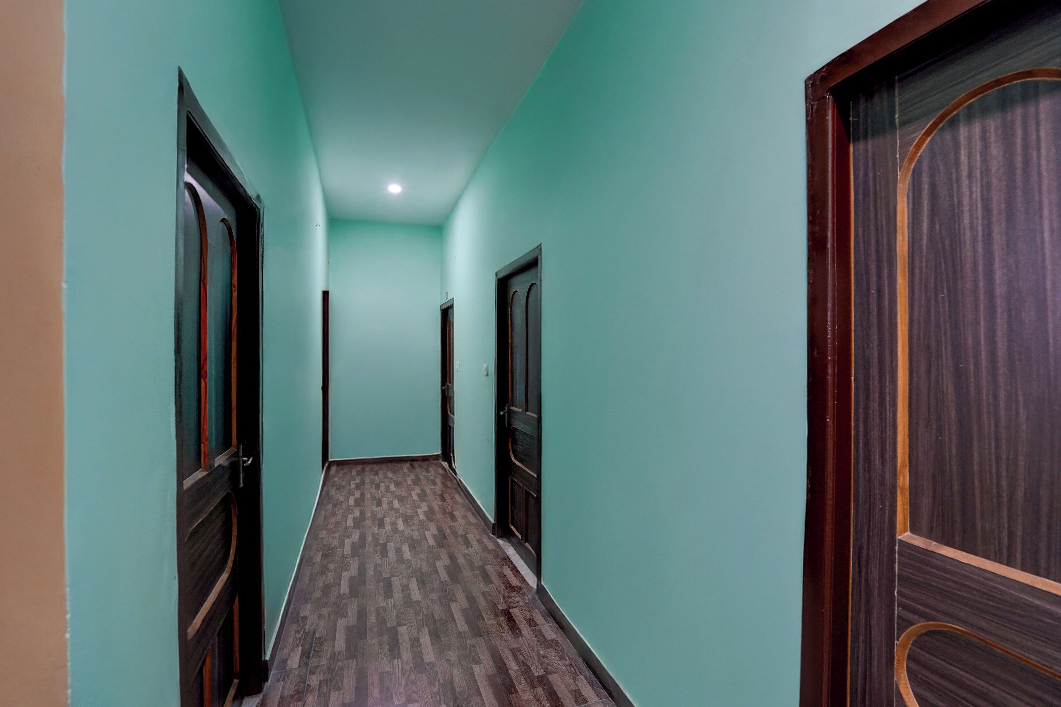 Un pasillo con paredes color turquesa y piso de madera, que conduce a una puerta de madera oscura al final.