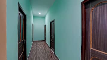 Un pasillo con paredes color turquesa y piso de madera, que conduce a una puerta de madera oscura al final.
