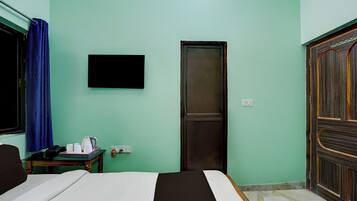 Una habitación de hotel con una cama, un escritorio con teléfono y hervidor, un televisor montado en la pared y un armario.