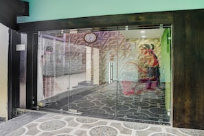 Entrada de um edifício com porta de vidro, um relógio e piso estampado.