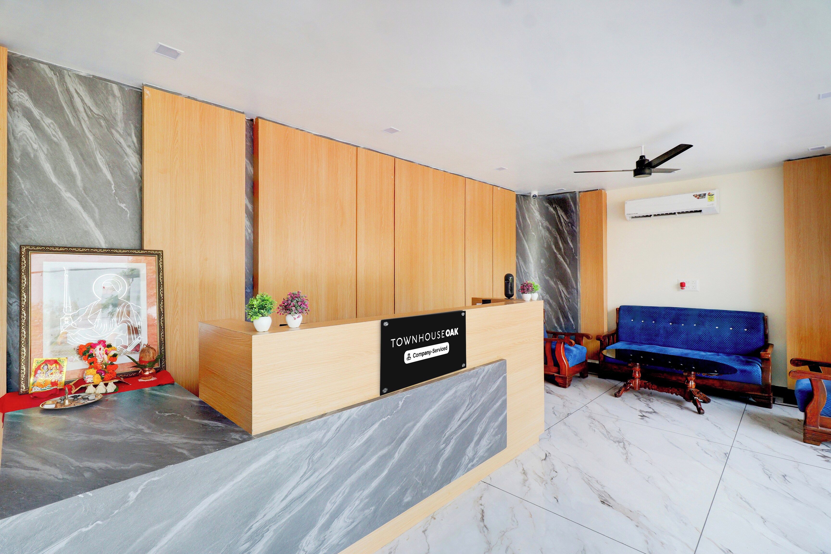 A reception area with a wooden reception desk, a blue sofa, and a ceiling fan.