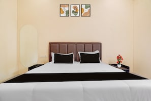 Una habitación de hotel con una cama, una mesita de noche con un jarrón de flores y tres cuadros en la pared.