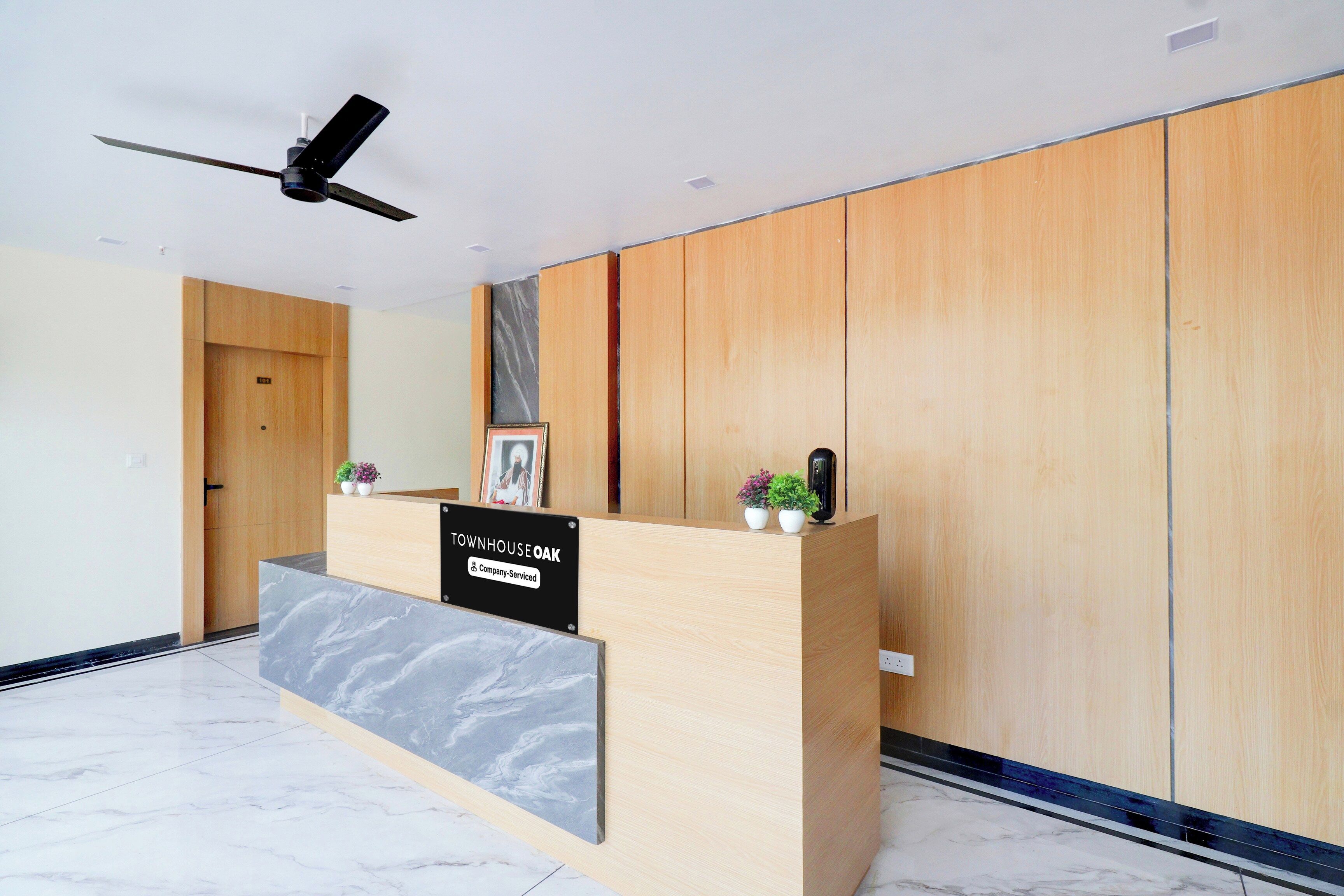 A reception desk with a marble top, wooden paneling on the walls, a ceiling fan, and a door labeled '101'.