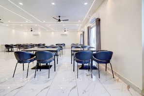 A conference room with a modern design, featuring marble flooring, rows of chairs, tables, ceiling fans, and air conditioning units.