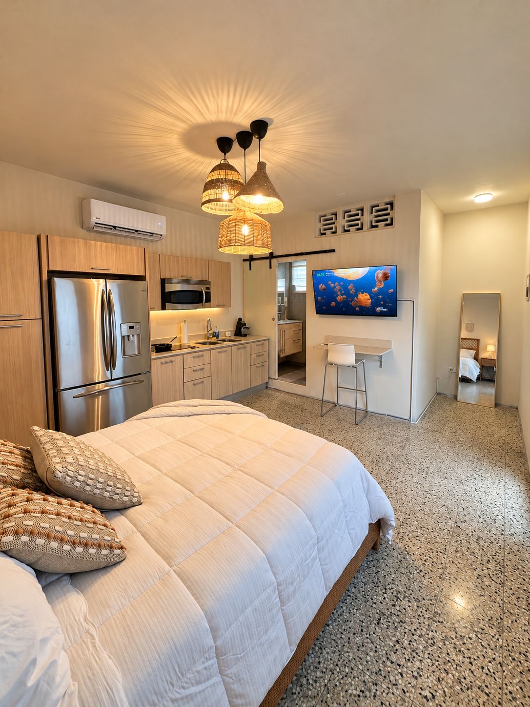 Une chambre moderne avec un grand lit, un coin cuisine et un téléviseur fixé au mur.