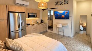 Une chambre moderne avec un grand lit, un coin cuisine et un téléviseur fixé au mur.