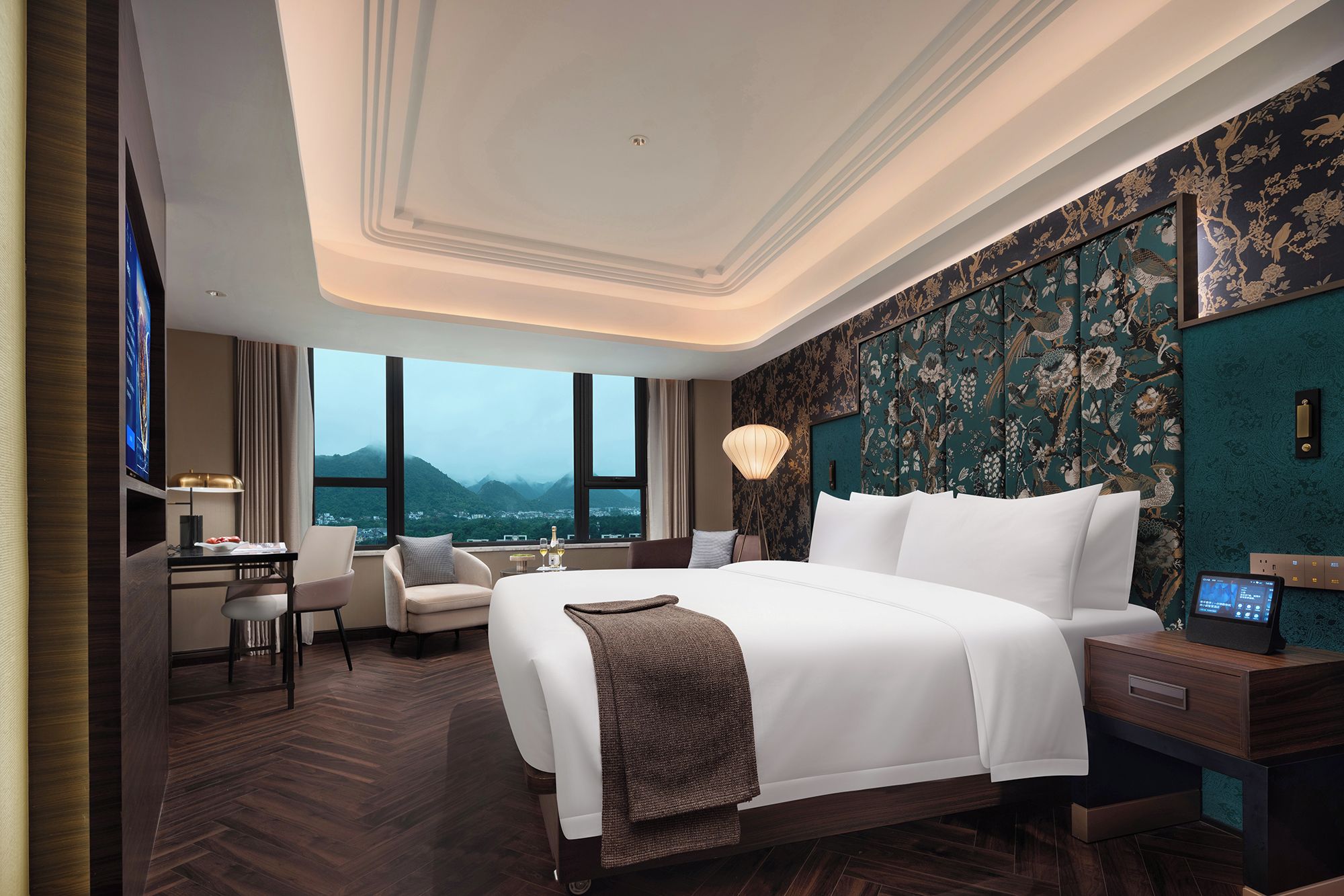 A hotel room with a large bed, a desk, and a view of mountains.