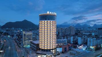 A modern hotel with a cylindrical design, surrounded by a cityscape and mountains in the background.