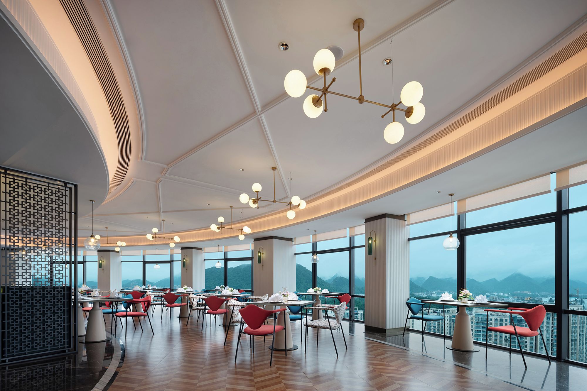 A modern dining area with multiple tables and chairs, large windows offering a mountain view, and contemporary lighting fixtures.