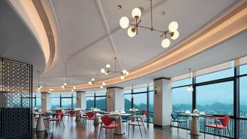 A modern dining area with multiple tables and chairs, large windows offering a mountain view, and contemporary lighting fixtures.