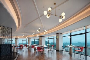 A modern dining area with multiple tables and chairs, large windows offering a mountain view, and contemporary lighting fixtures. - Metropolo Jinjiang Guilin Rail St Mixc (guilin)