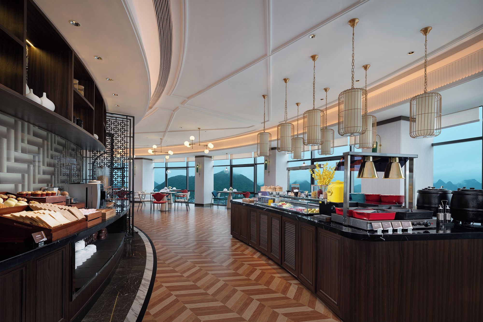 A modern hotel lobby with a central bar area, seating arrangements, and large windows offering a view of the mountains.