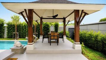 A covered outdoor seating area with a pool, wooden furniture, and a pergola structure.